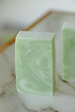 Load image into Gallery viewer, A light green bar of coconut milk and aloe soap rests on a table.
