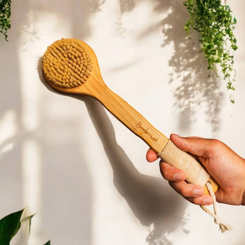 A hand holding a bamboo dry brush, with has a cotton loop for hanging