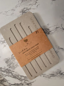 A grey, diatomite shampoo and conditioner tray rests on a marble surface. 