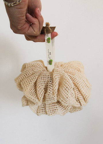 Hand holding a beige shower pouf by the loop 