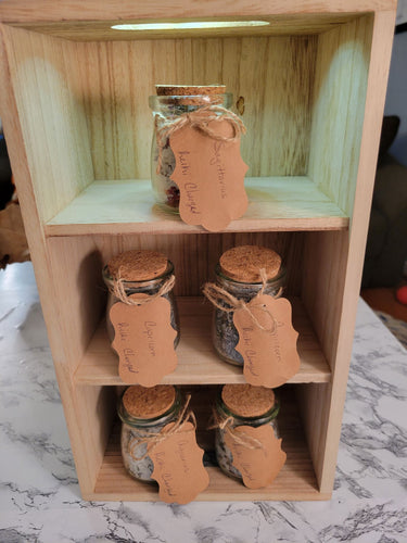 Zodiac-inspired, reiki-charged bath salts in small glass jars displayed on a wooden shelf.
