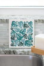 Load image into Gallery viewer, A swedish dishcloth with a monstera leaf pattern resting on a sink
