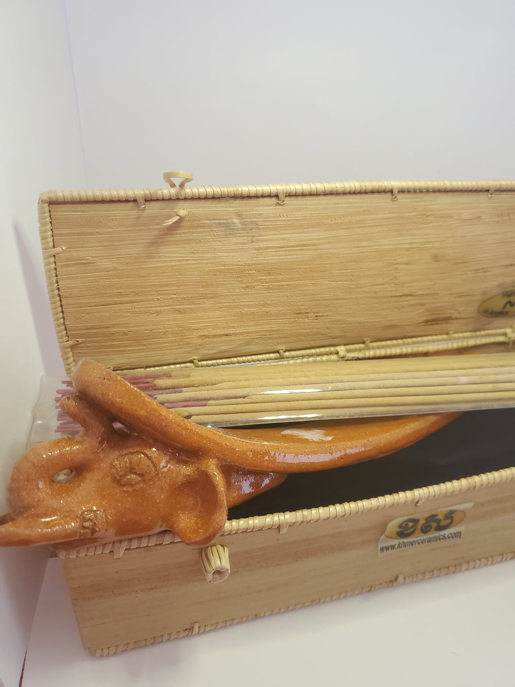 An orange elephant shaped incense burner pokes out of a bamboo box. Some incense rest on top. 