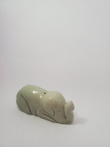 A small, light green elephant incense holder on a white background. The elephant appears to be curled up with its trunk up. THere is a small hole for a stick insence 