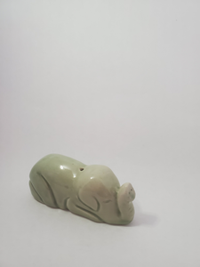 A small, light green elephant incense holder on a white background. The elephant appears to be curled up with its trunk up. THere is a small hole for a stick insence 