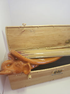 An orange, handmade, elephant shaped incense burner pokes out of a bamboo box. Some incense rest on top.  Handmade in Siam Reap, Cambodia.